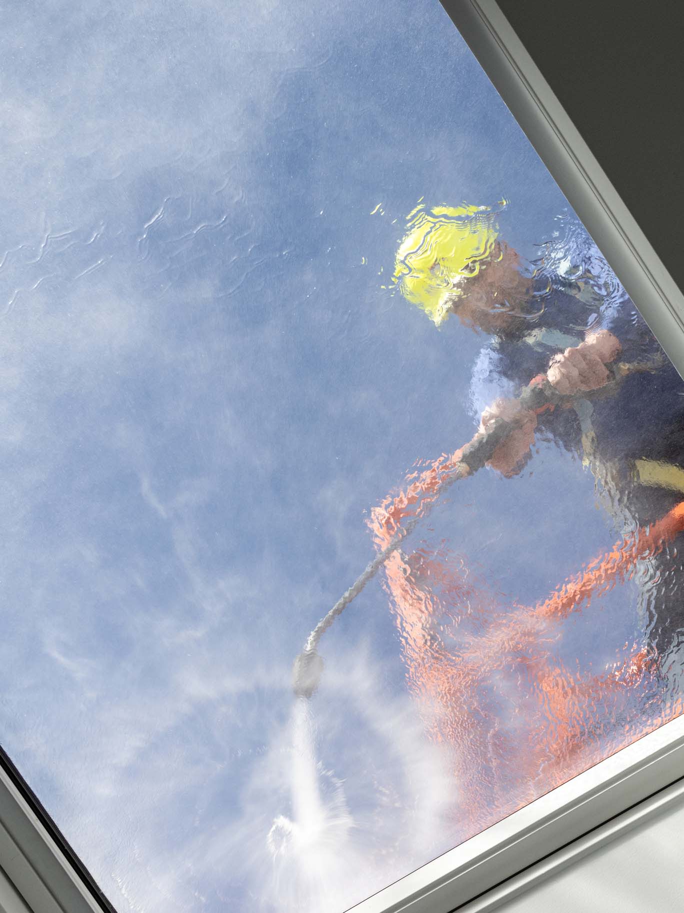 Worker on a cherry picker cleaning a roof windows with high pressure water jet. Low angle shot